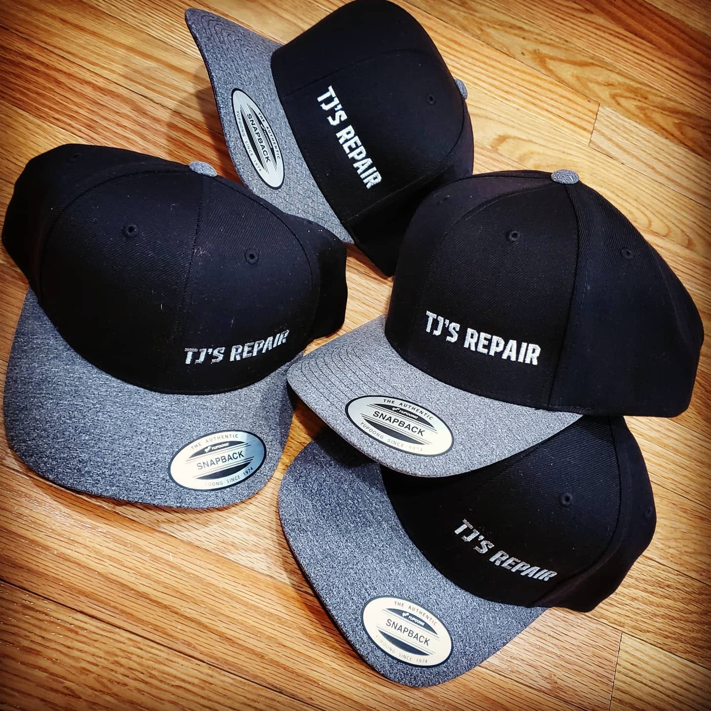 Black and gray snapback hats embroidered with TJ's Repair