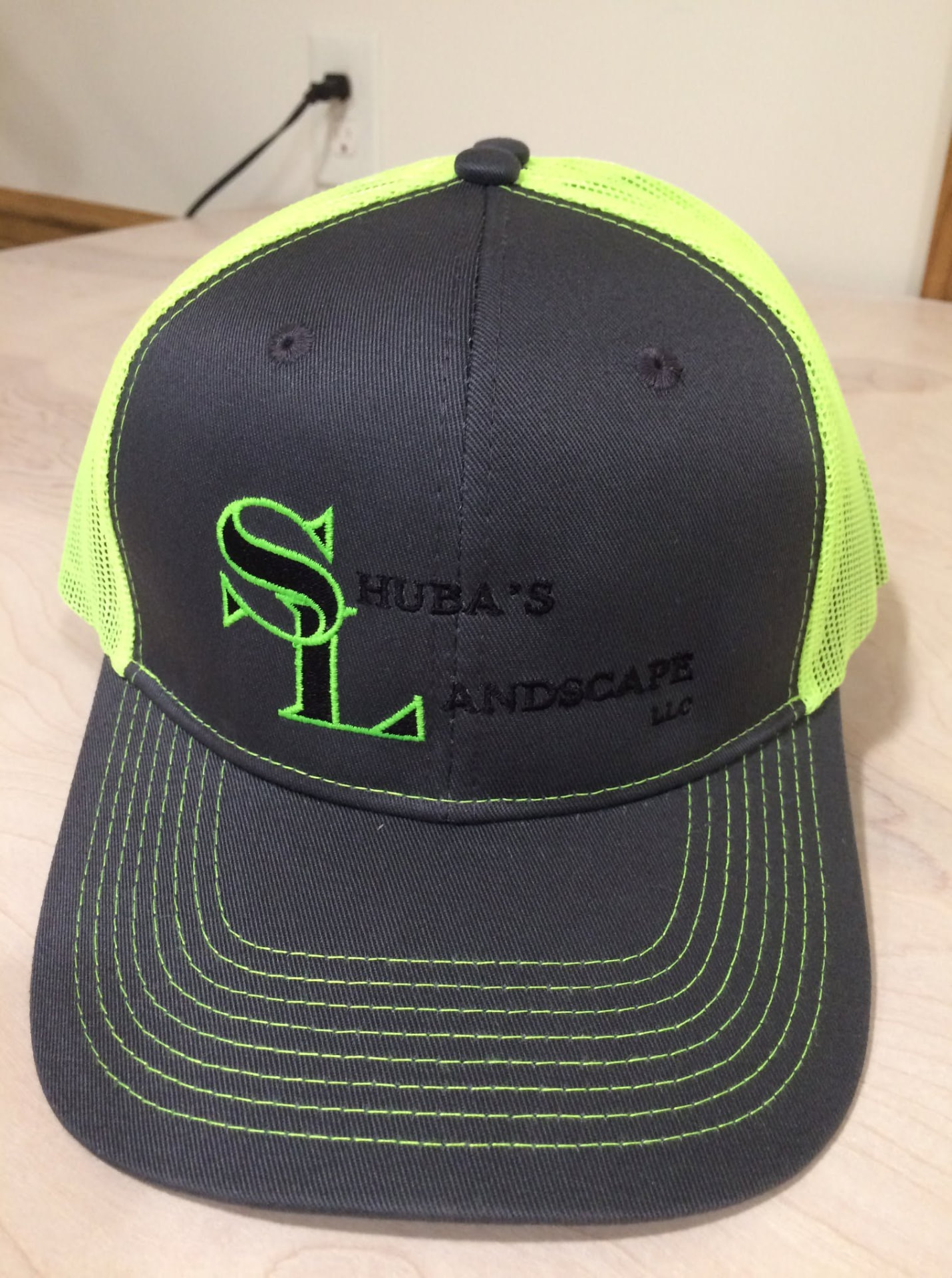 Charcoal and neon green trucker hat embroidered with Shuba's Landscape logo